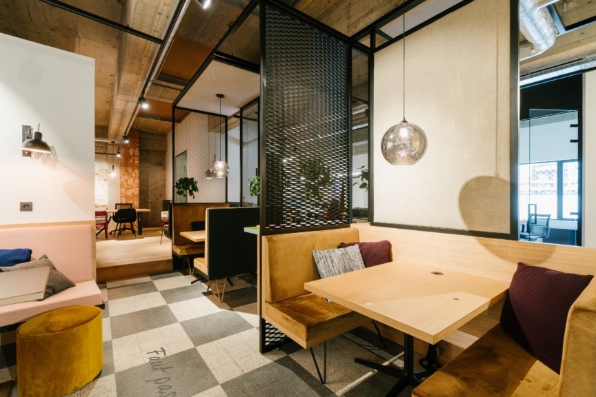 Modern coworking space with booth seating, wood tables, pendant lights, and industrial design elements.