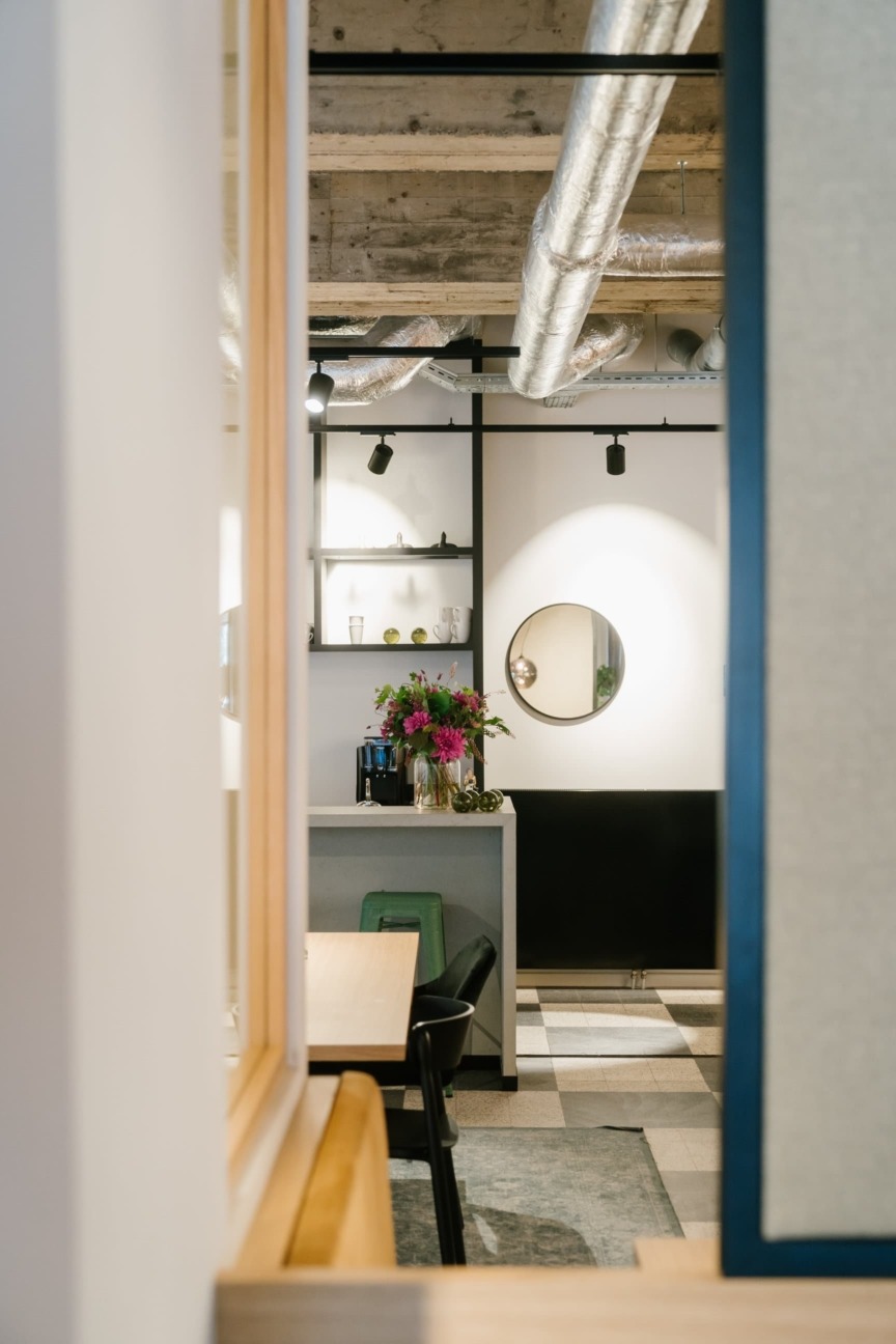 Modern interior with a cozy vibe, featuring exposed ductwork, a dining area, a small bar with fresh flowers, and a round mirror on the wall.
